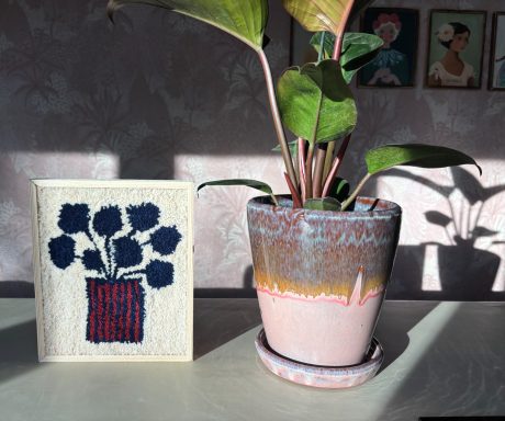 Laura Tuftschilderij met creme kleurig achtergrond en vaas met strepen blauw/bordeaux. Bordeaux kleurige bloemen.