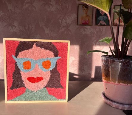 Tracy Portret van een vrouw met een lichte huid en een trendy zonnebril, op een tafel met een plant.
