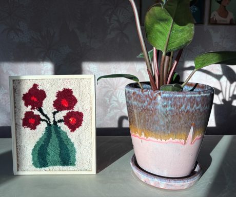 Maartje Tuftschilderij met witte achtergrond met bloemenvaas in groen en bordeaux kleurige bloemen.