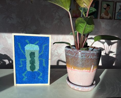 Mae Tuftschilderij met een blauwe achtergrond met een groen insedct erop.