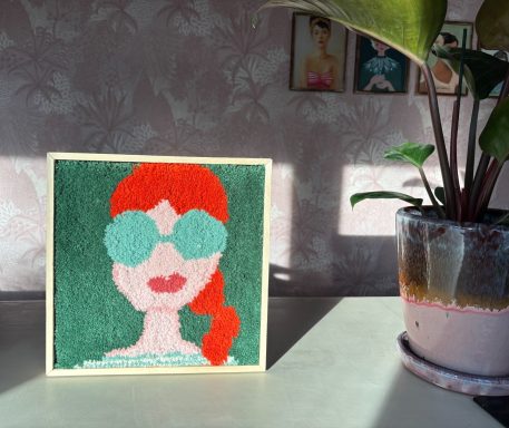 Nina Vrolijk tuftwerk van een vrouw met rode haren en grote zonnebril.