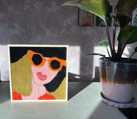 Cleo Een kleurrijke wanddecoratie van een vrouw met oranje zonnebril en een plant op de achtergrond.